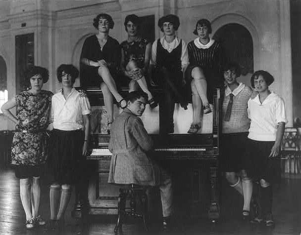 Group of flappers and man seated at a piano